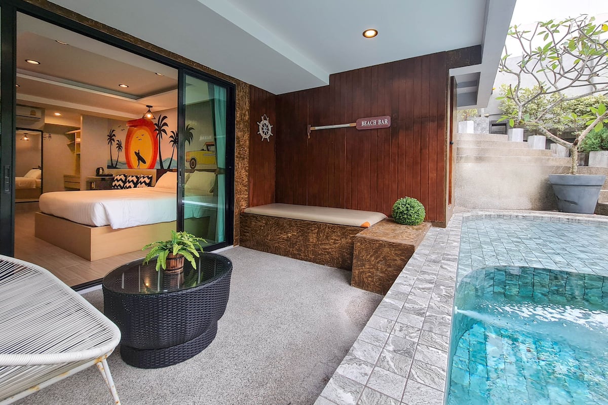 Habitació d'hotel moderna amb un llit, zona de seients, taula petita amb una planta i vista a una piscina.