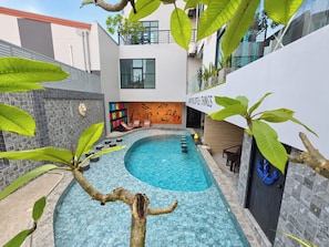Un espace piscine intérieur moderne, avec une piscine à l’eau cristalline, des chaises longues et un mur orné d’œuvres d’art colorées.