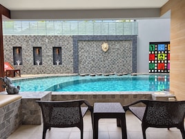 Una piscina con paredes de piedra y una decoración de cabeza de león, rodeada de sillas de mimbre y un suelo de baldosas.