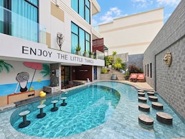 Zona de piscina con un mural, sillones de descanso y un cartel que dice 'ENJOY THE LITTLE THINGS'.
