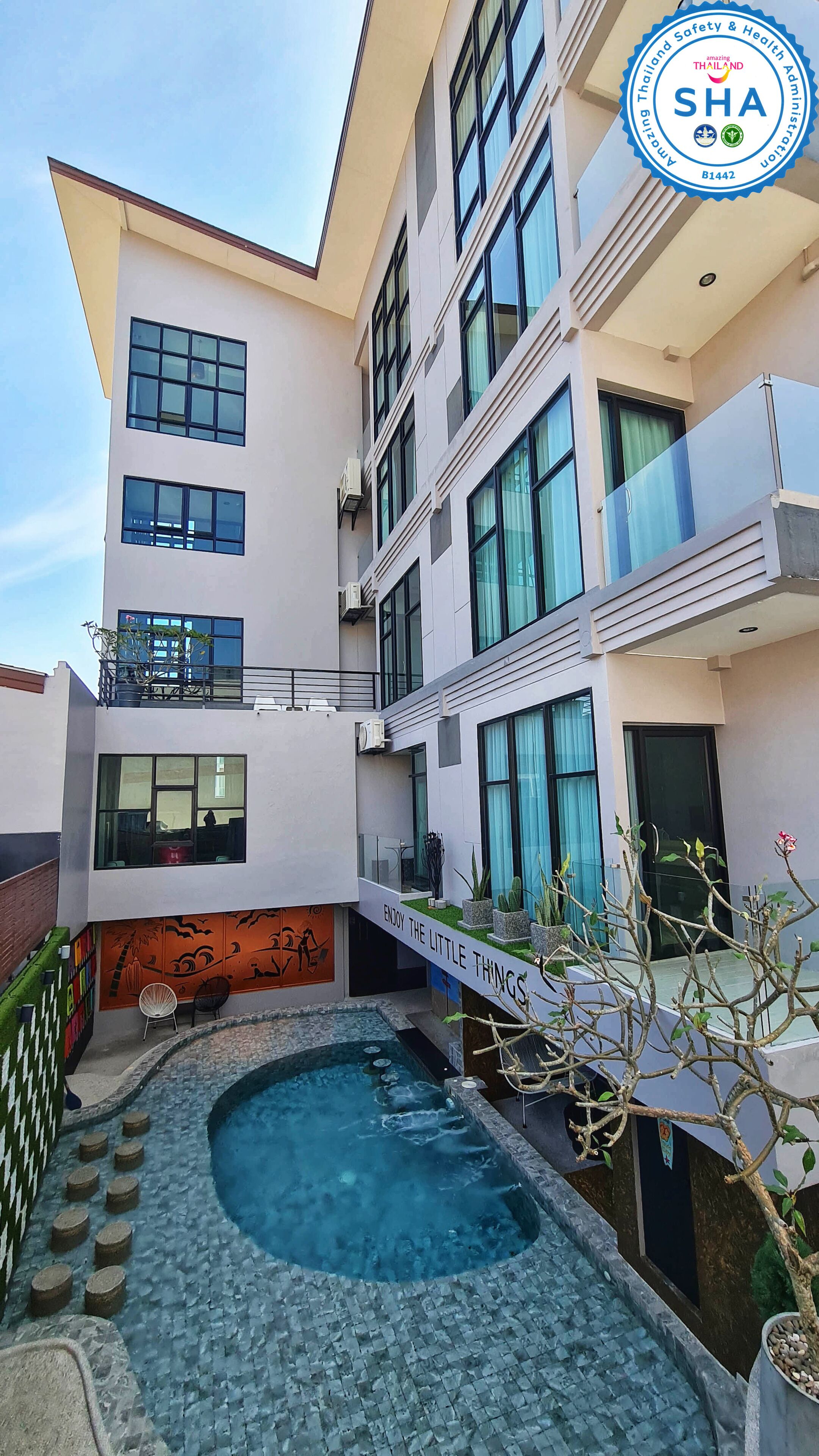 A modern building with a rooftop pool, multiple balconies, and a sign that reads "ENJOY THE LITTLE THINGS."