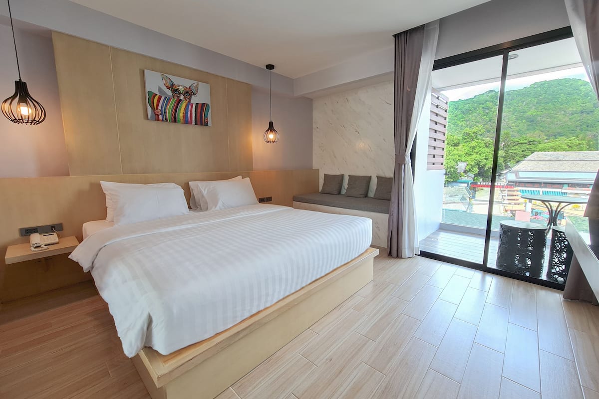 Habitació d'hotel moderna amb un llit gran, taules de nit, un quadre i vistes a un edifici i vegetació.