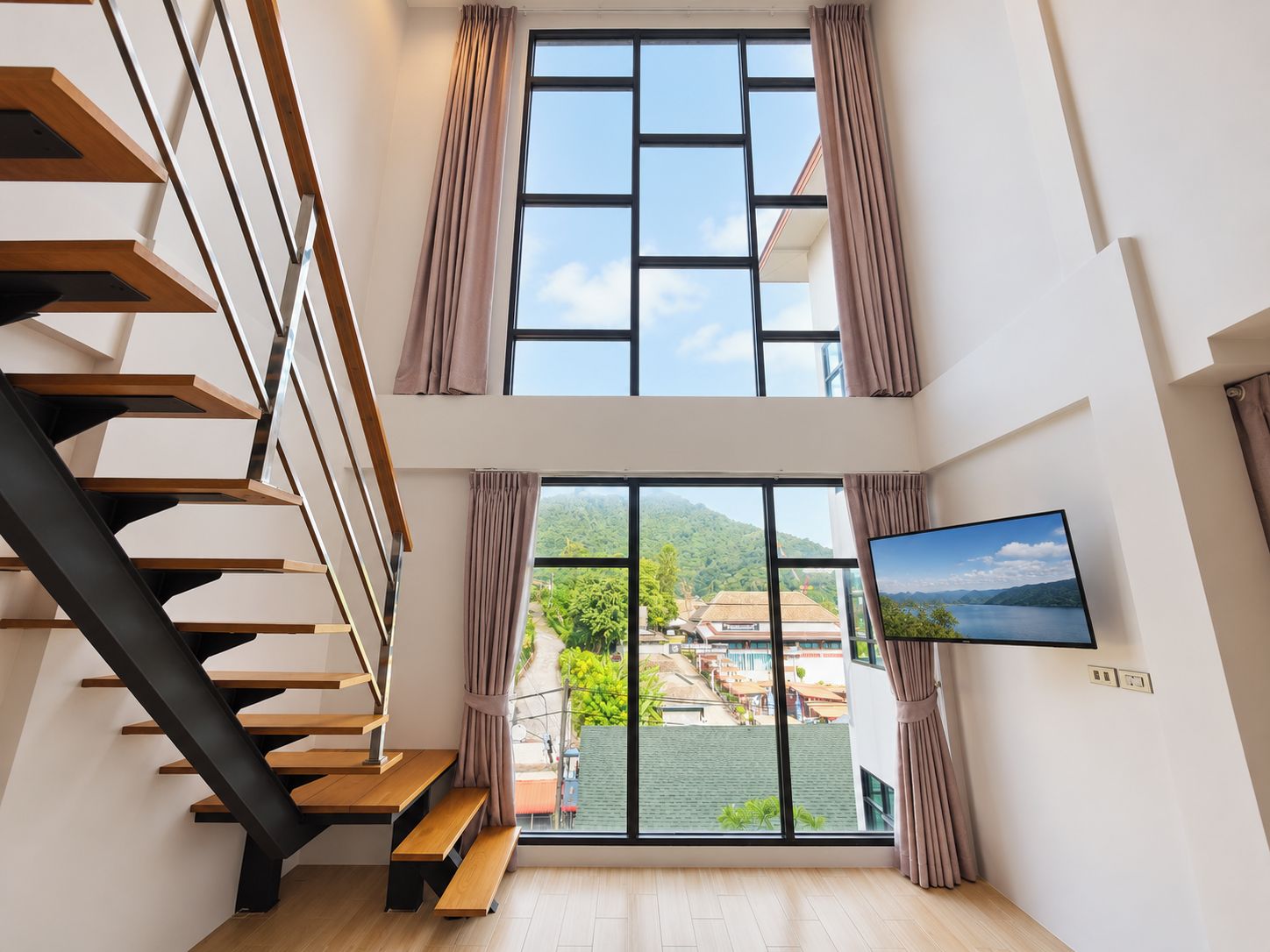 A modern interior with a staircase, large windows, and a view of a green landscape.