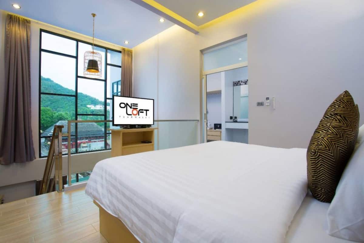 Habitació d'hotel moderna amb un llit gran, una televisió, una finestra amb vista a vegetació i un mirall.