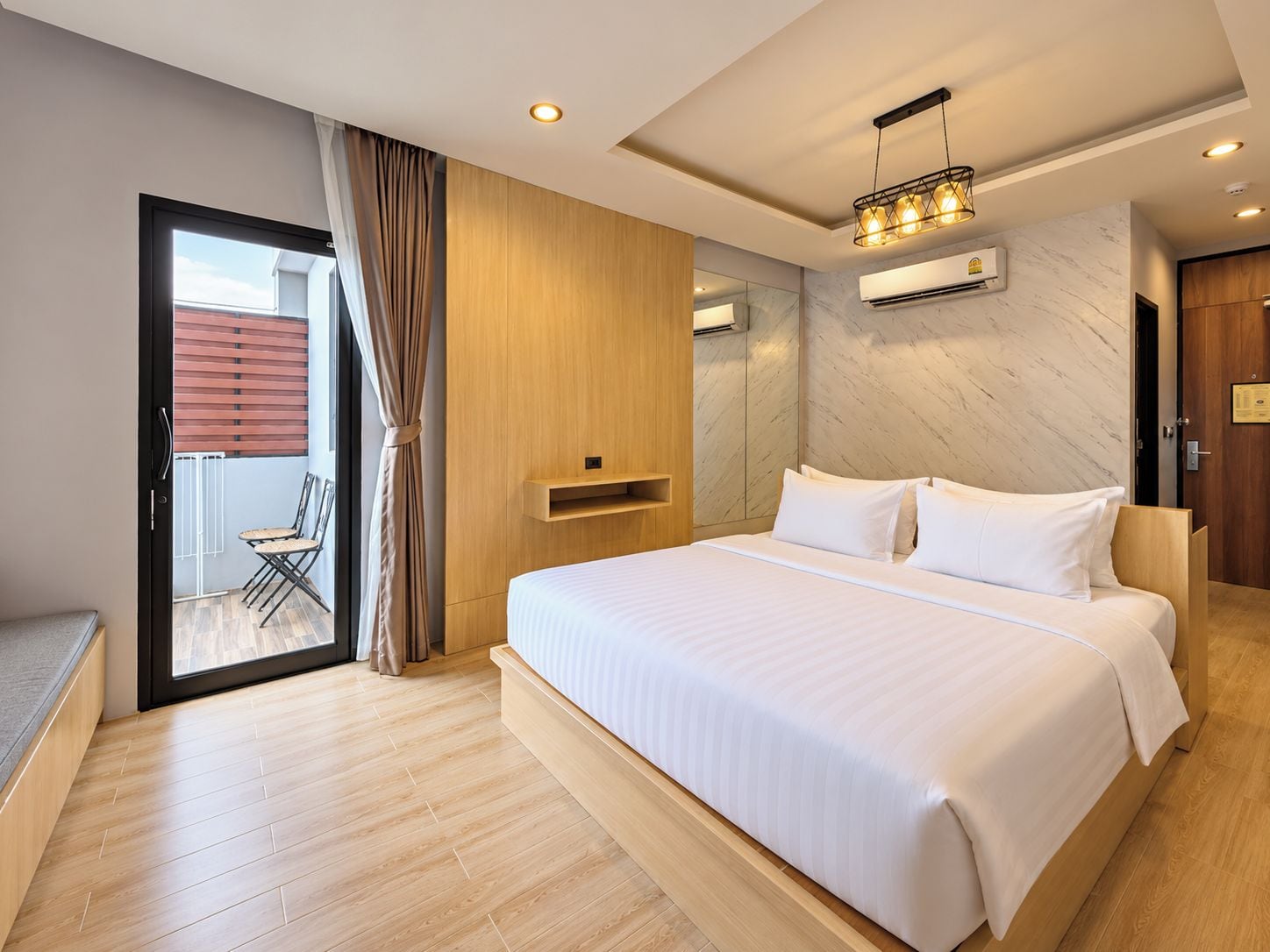 A modern hotel room with a large bed, a sliding glass door to a balcony, and a built-in air conditioning unit.