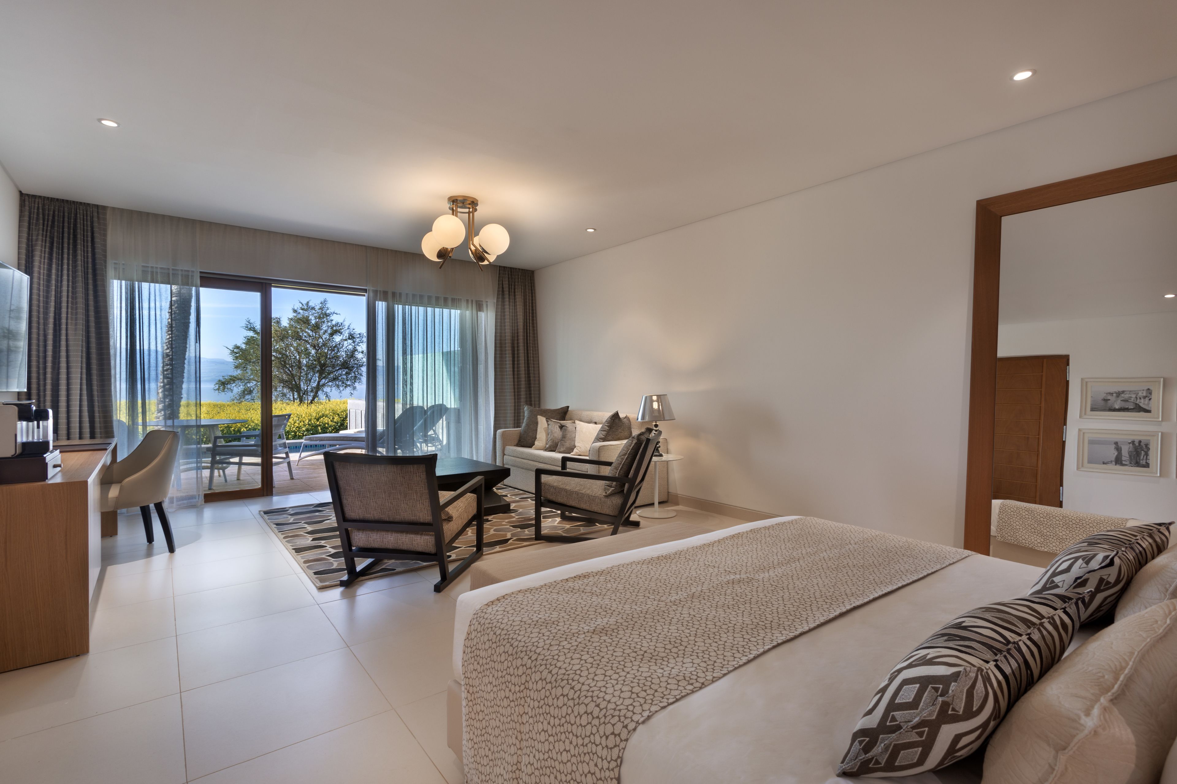 A modern hotel room with a large bed, a desk, and a seating area with a view of the outdoors.