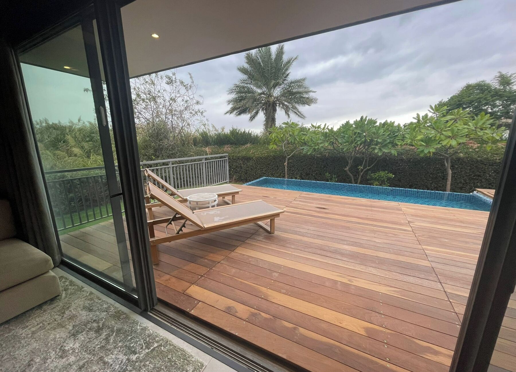 A wooden deck with a pool, a lounge chair, and a glass door leading to a balcony.
