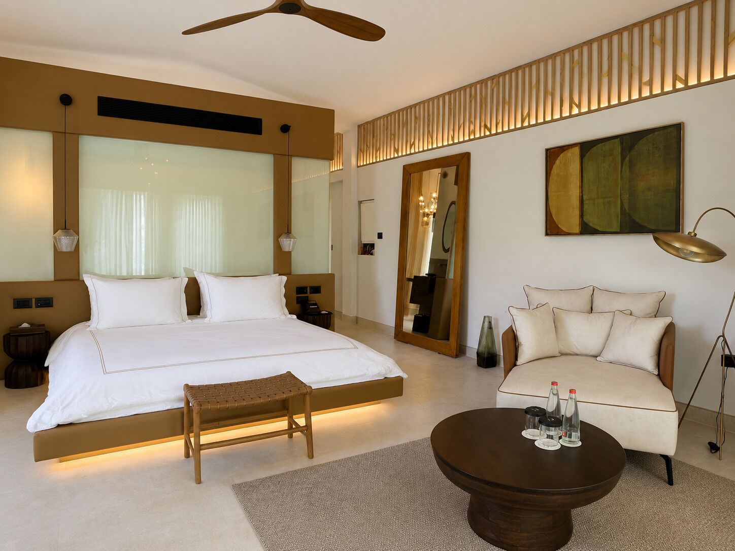 A modern hotel room with a large bed, a sofa, a coffee table, and a mirror.