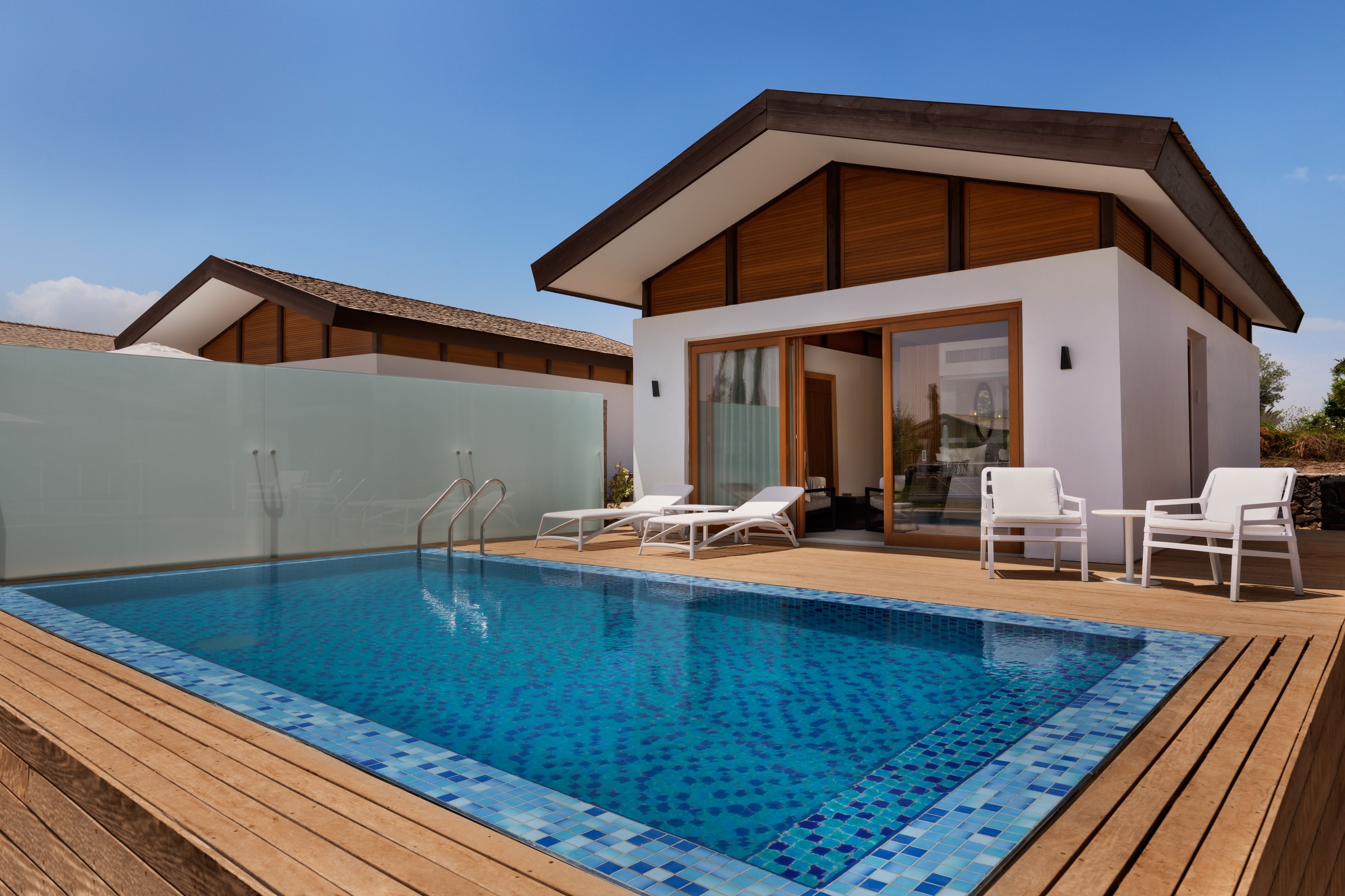 A modern pool area with a clear blue pool, wooden deck, and white lounge chairs.