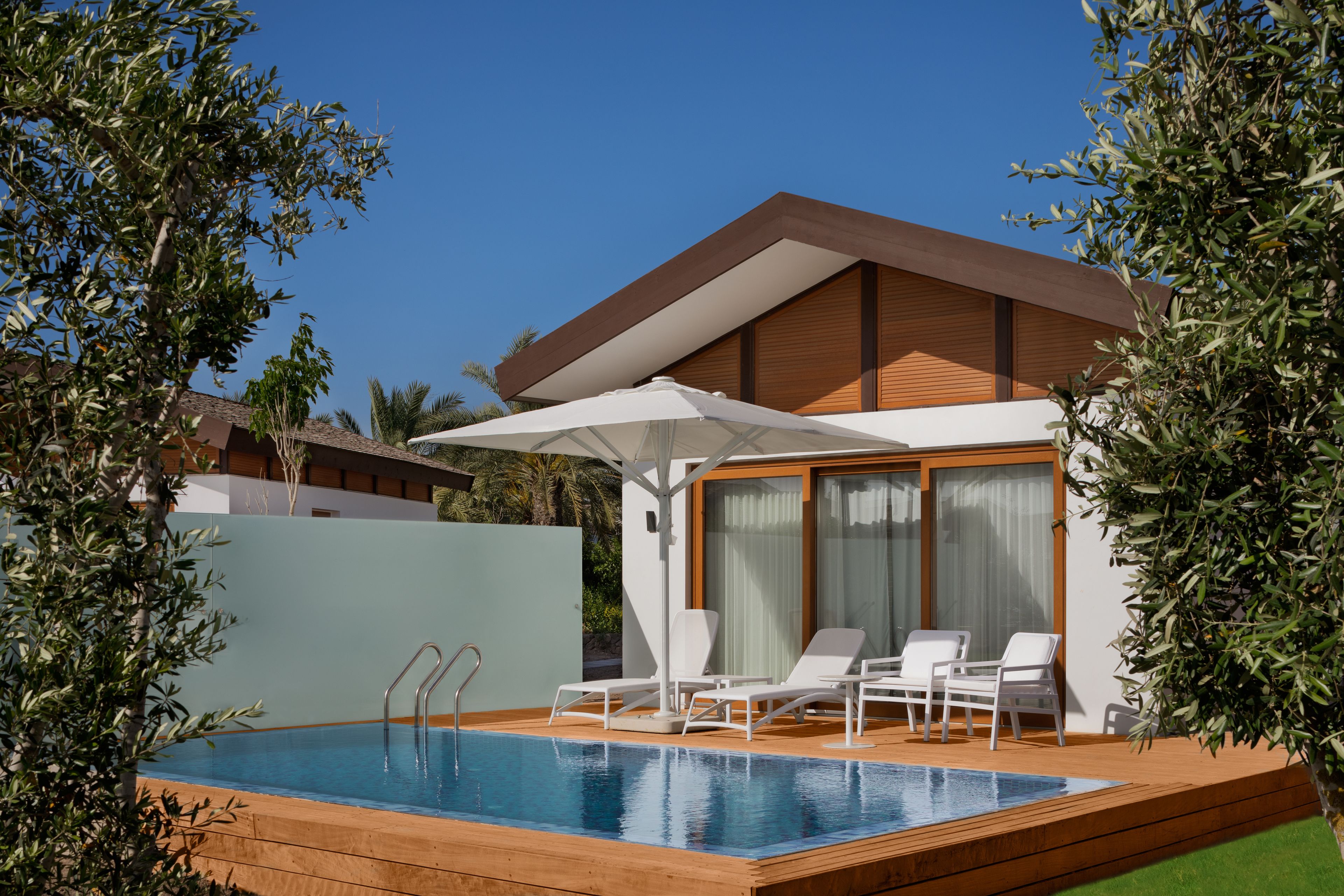 A modern pool area with a wooden deck, two lounge chairs, and a large umbrella.