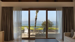 A room with a sliding glass door leading to an outdoor patio with a table and chairs, a sofa, and a view of a landscape with mountains and a body of water. - The Setai Sea of Galilee (Ramot)