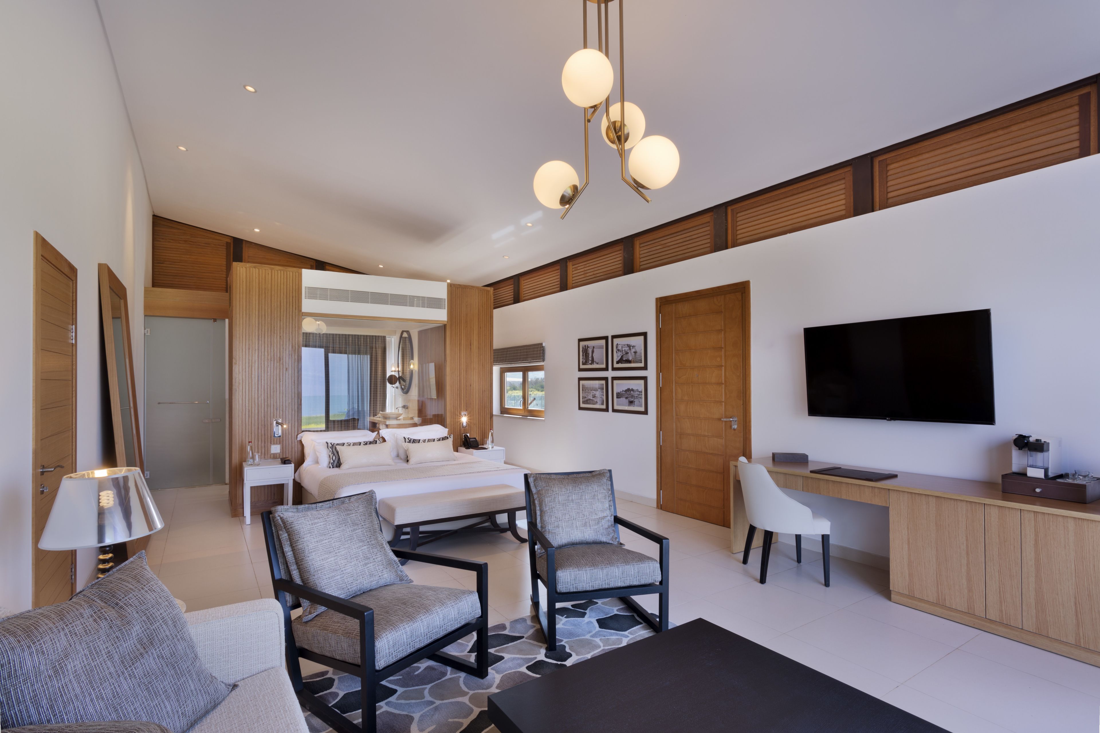 A modern hotel room with a large bed, two armchairs, a desk, and a TV.