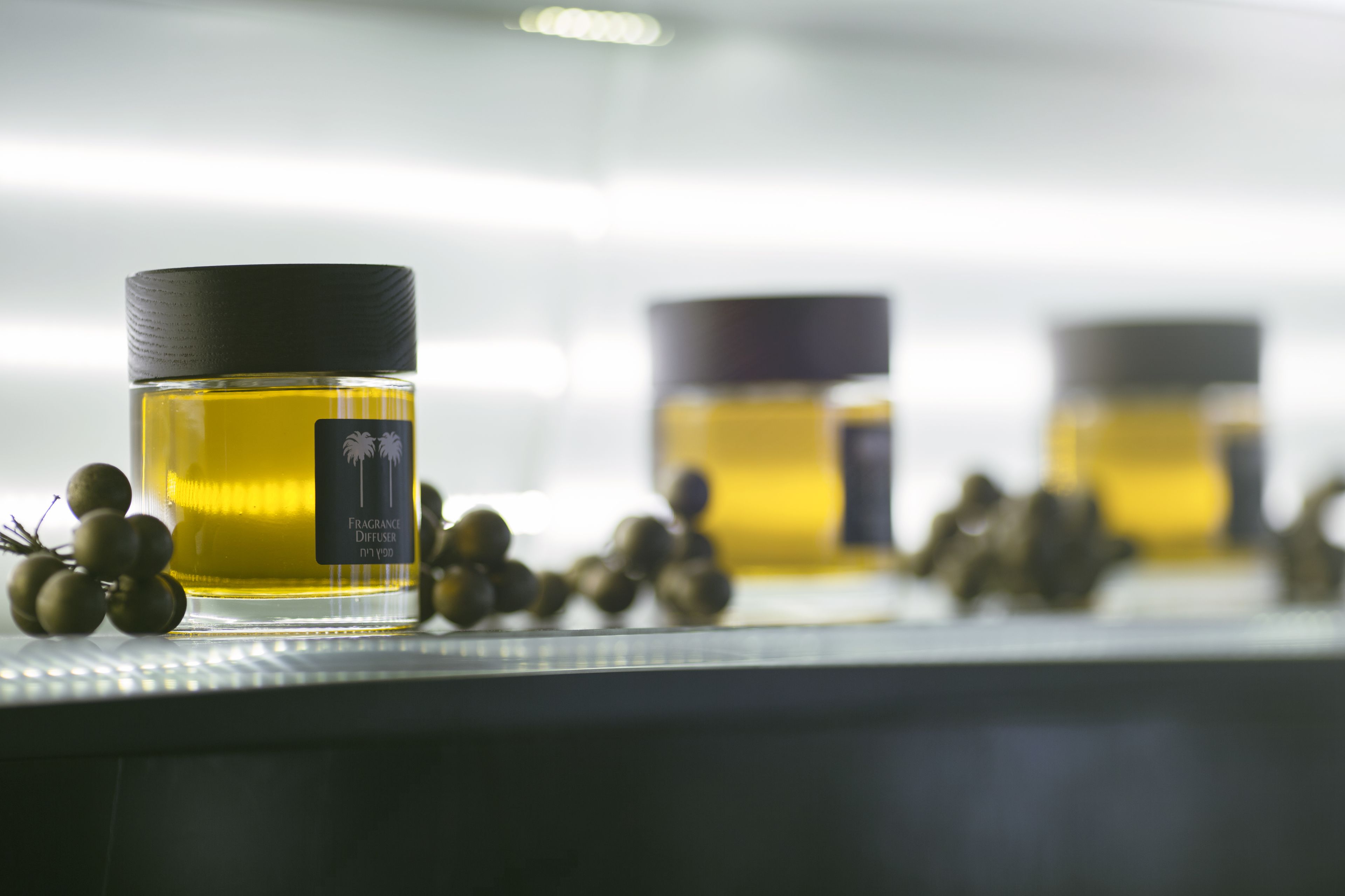 Una fila de frascos de perfume con tapones negros, cada uno con una etiqueta, y algunas uvas sobre una superficie reflectante.