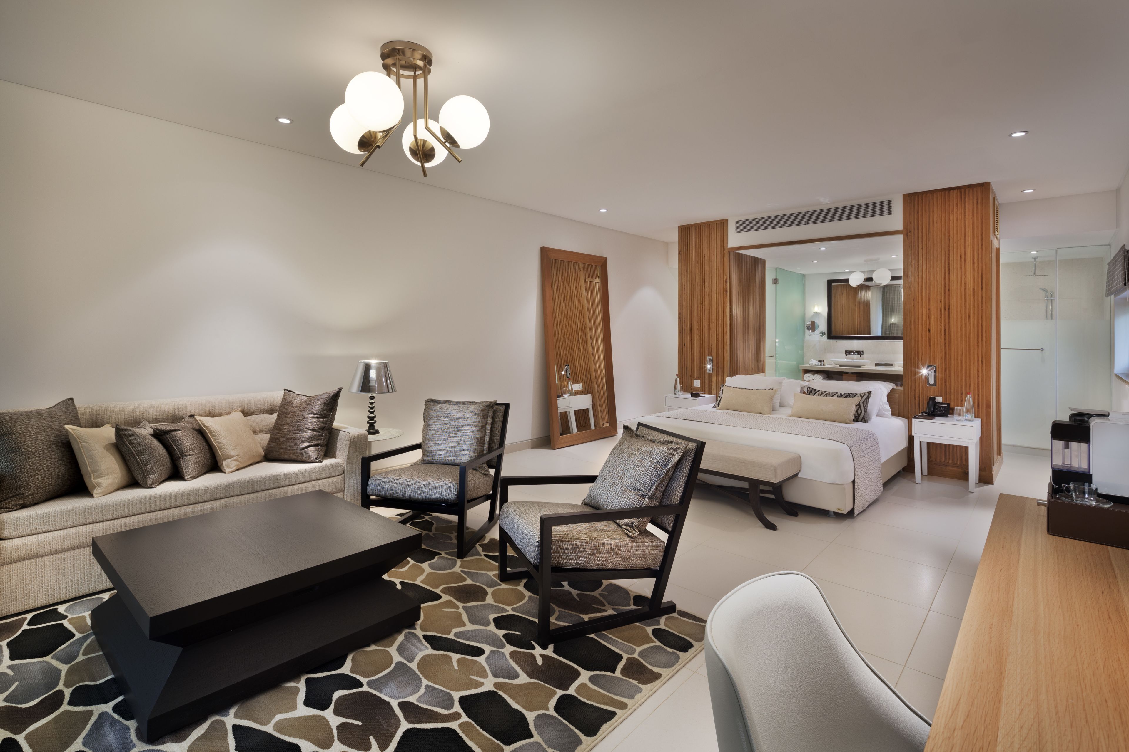 Une chambre d’hôtel moderne équipée d’un canapé, de fauteuils, d’une table basse, d’un lit, d’un bureau et d’un miroir.