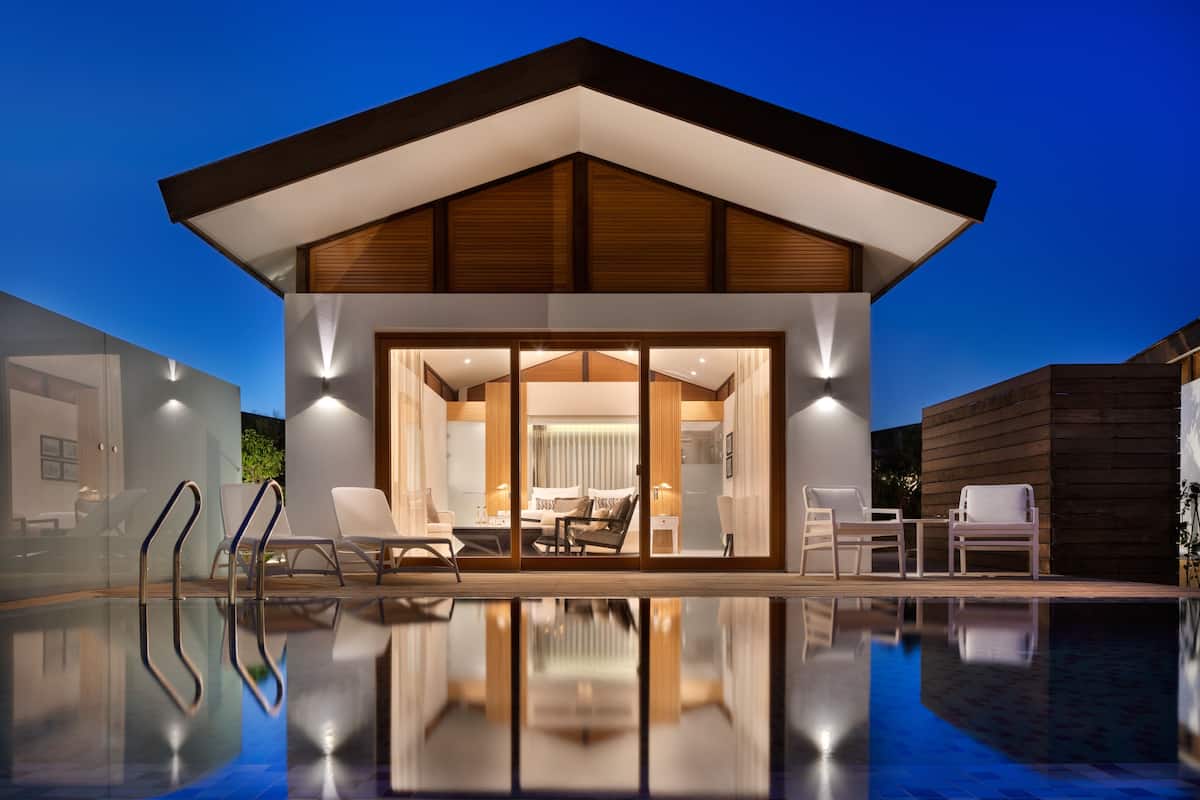 A modern building with a pool, glass doors, and a lounge area with chairs and a table.