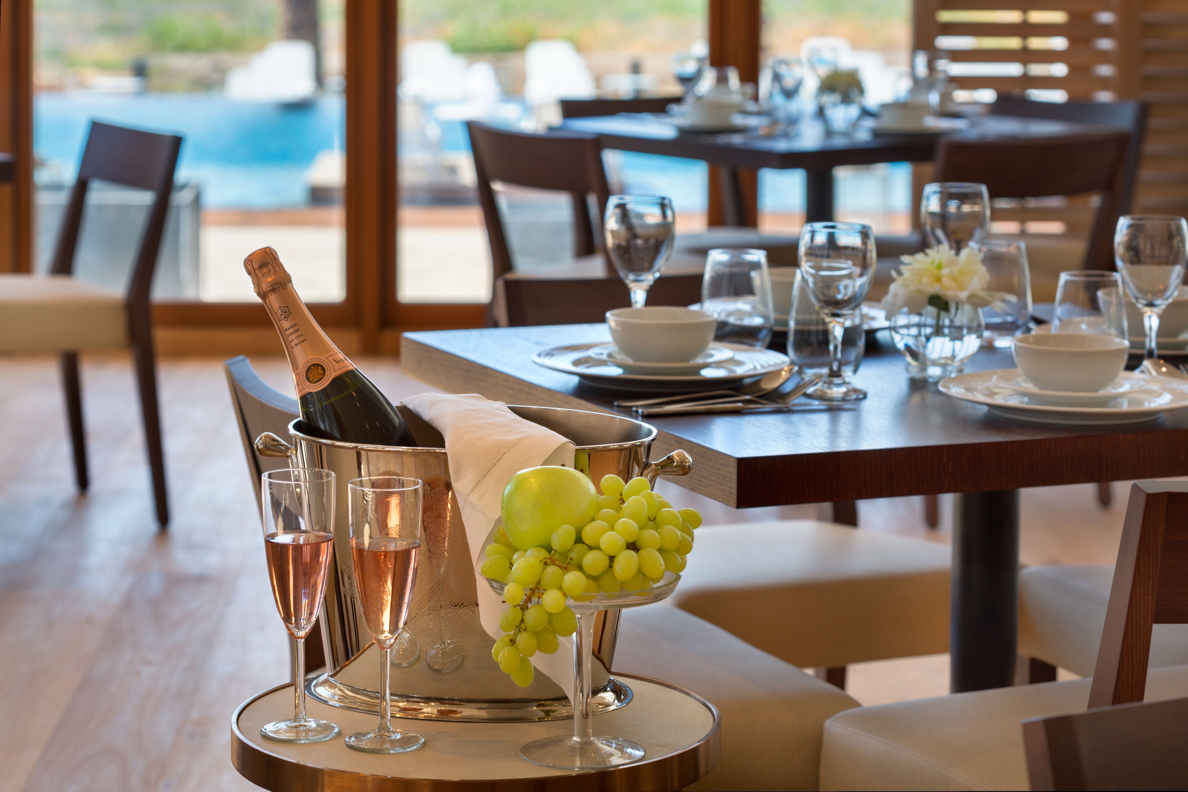 A dining table set with wine glasses, a bottle of champagne, and a bowl of grapes.