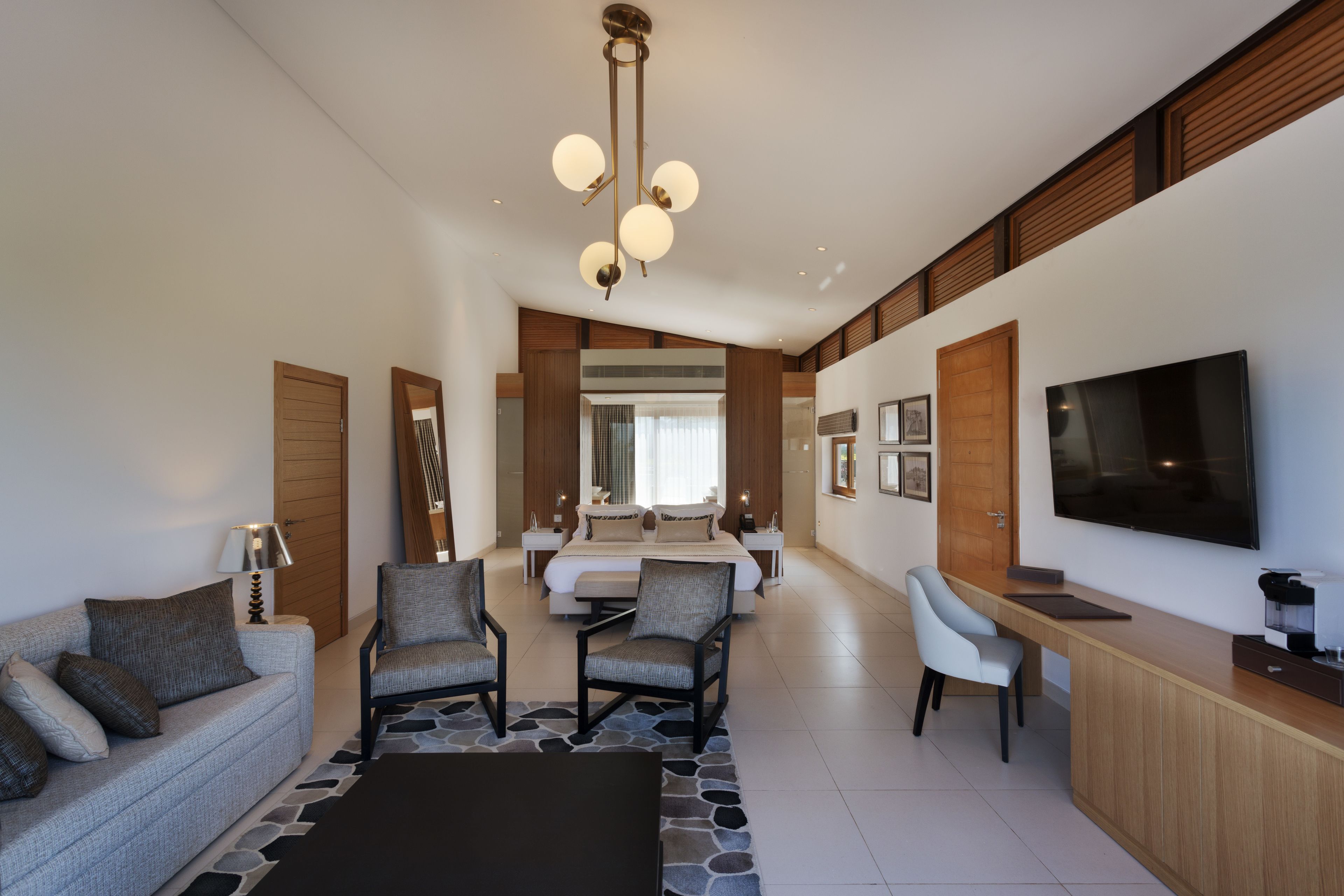 Une chambre d’hôtel moderne équipée d’un lit, d’un canapé, de deux fauteuils, d’un bureau et d’une télévision.