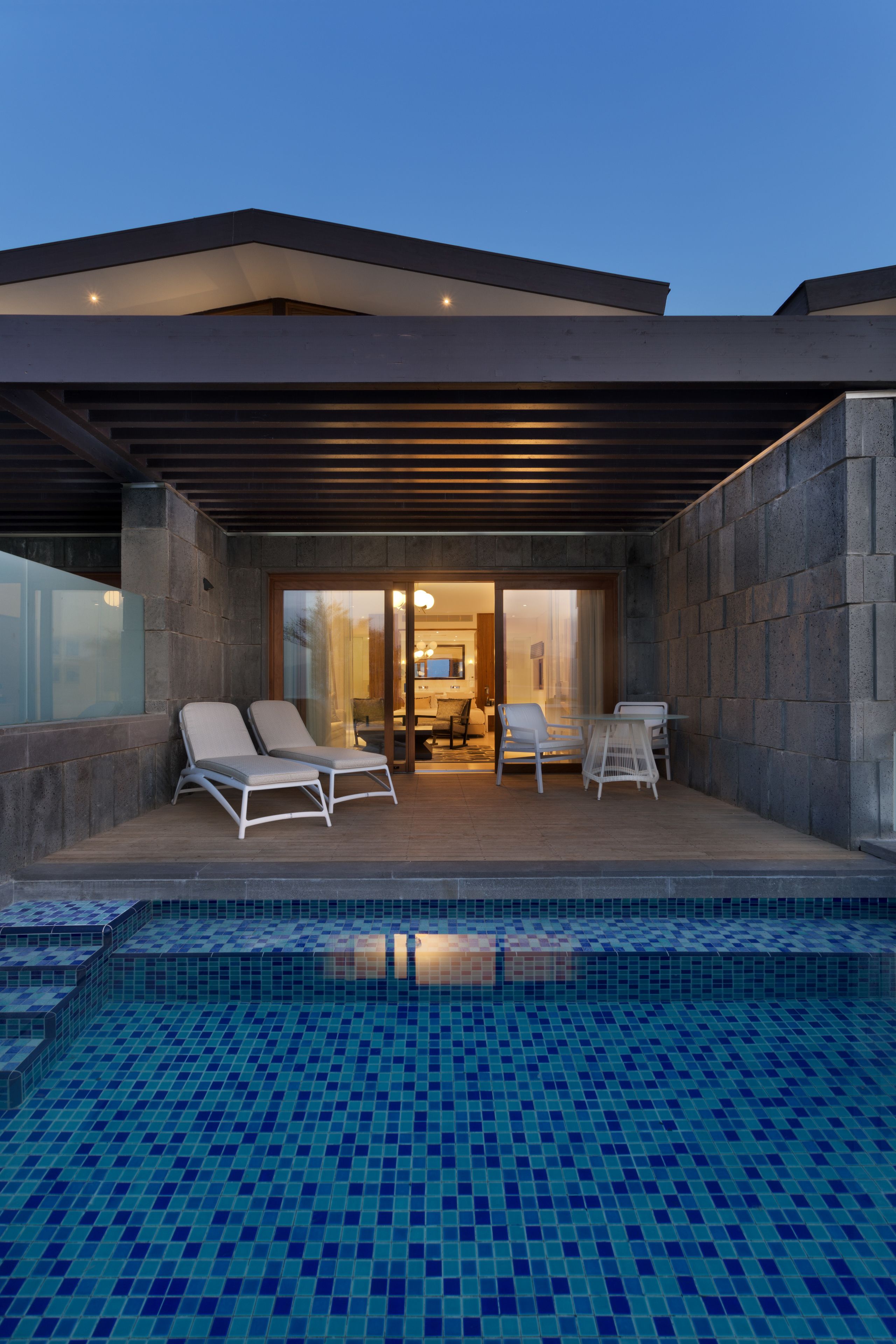 A modern outdoor pool area with lounge chairs and a covered seating area.