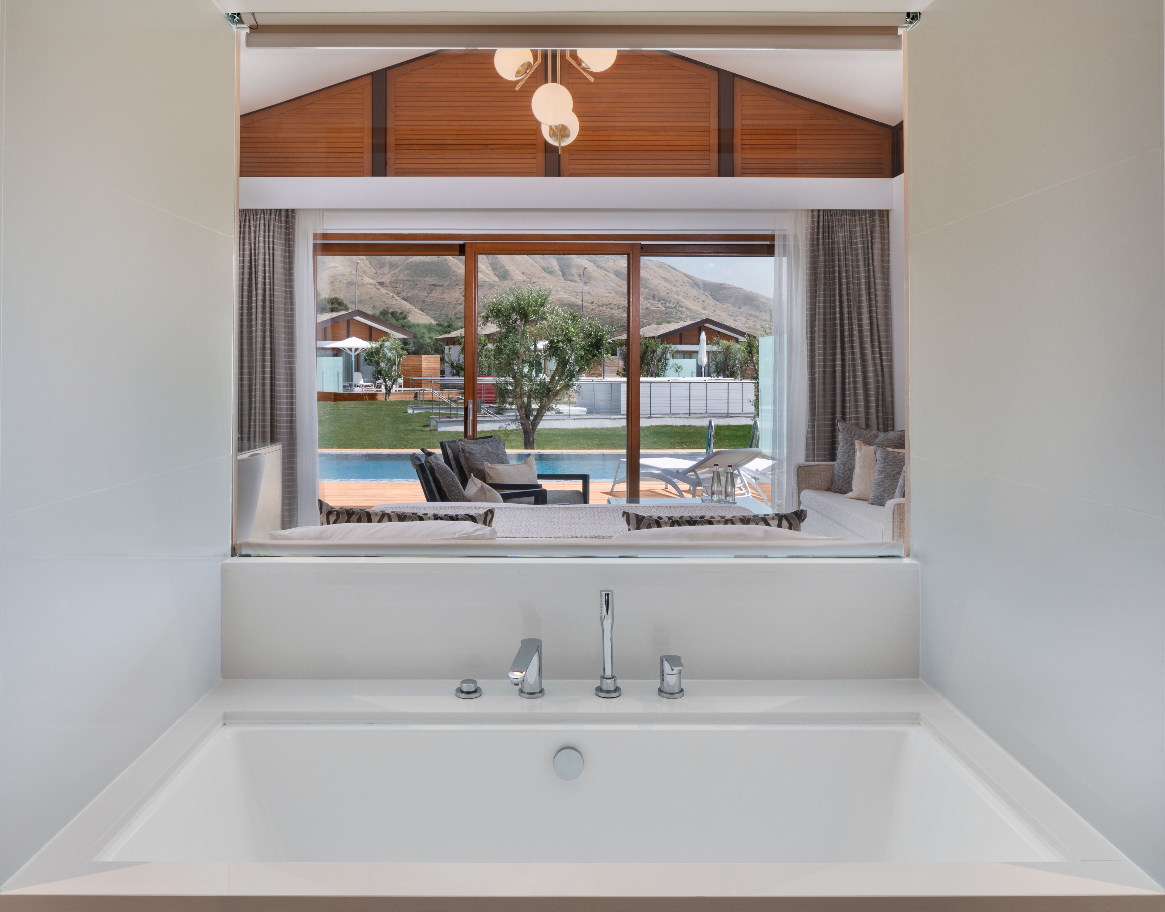 A modern bathroom with a large bathtub, a window overlooking a pool and outdoor seating area.