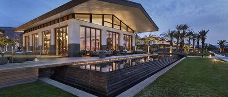 Una casa moderna con una amplia terraza, piscina y césped cuidado.
