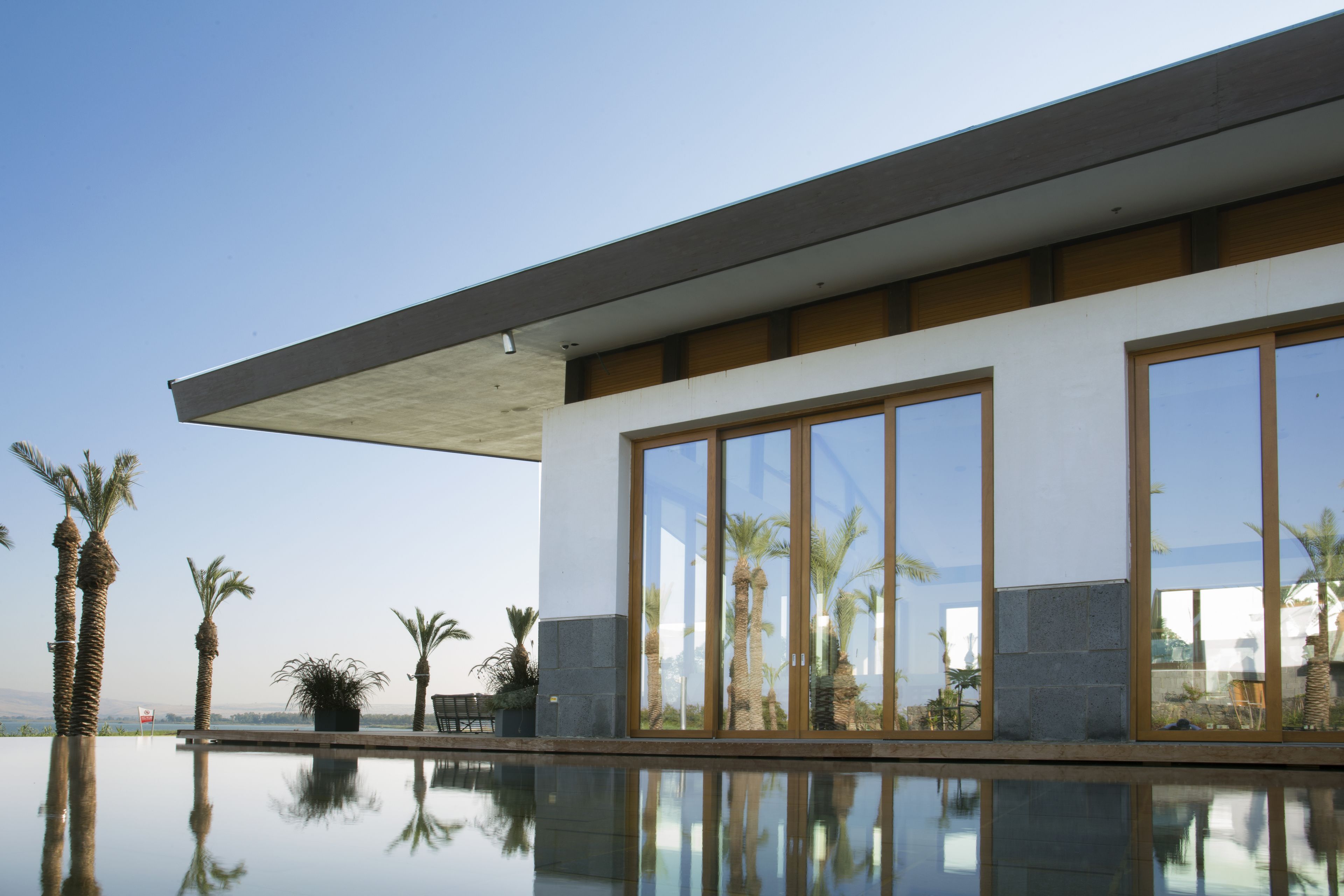 A modern building with large windows reflecting palm trees and a clear sky.