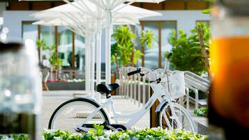 Una bicicleta blanca estacionada bajo sombrillas blancas, con follaje y un edificio al fondo.