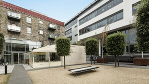 Un patio con un banco, una zona de estar cubierta y un edificio con fachada de piedra y entrada de vidrio moderna.