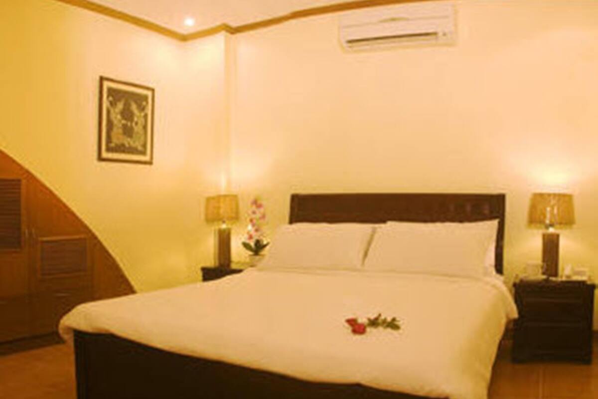 A hotel room with a large bed, two bedside tables with lamps, a wall-mounted air conditioner, and a framed picture on the wall.