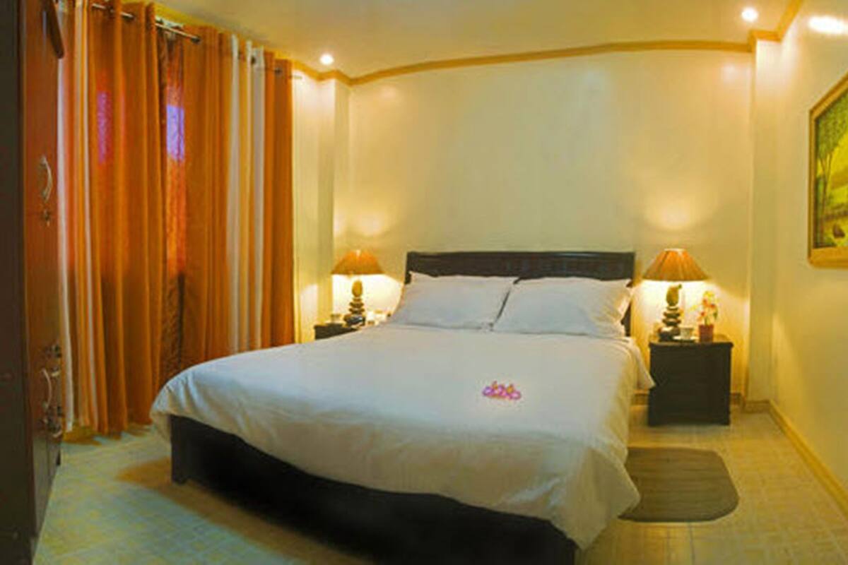 A hotel room with a large bed, two bedside tables with lamps, a painting on the wall, and a curtain on the window.