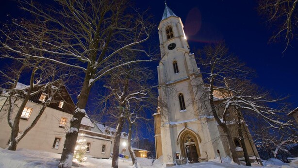A snow-covered church with a tall bell tower and a lit-up facade. - Hotel Miriquidi (Oberwiesenthal)