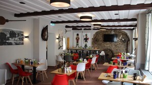 A restaurant with multiple tables and chairs, a stone wall with a TV, and various wall decorations. - Hotel Miriquidi (Oberwiesenthal)