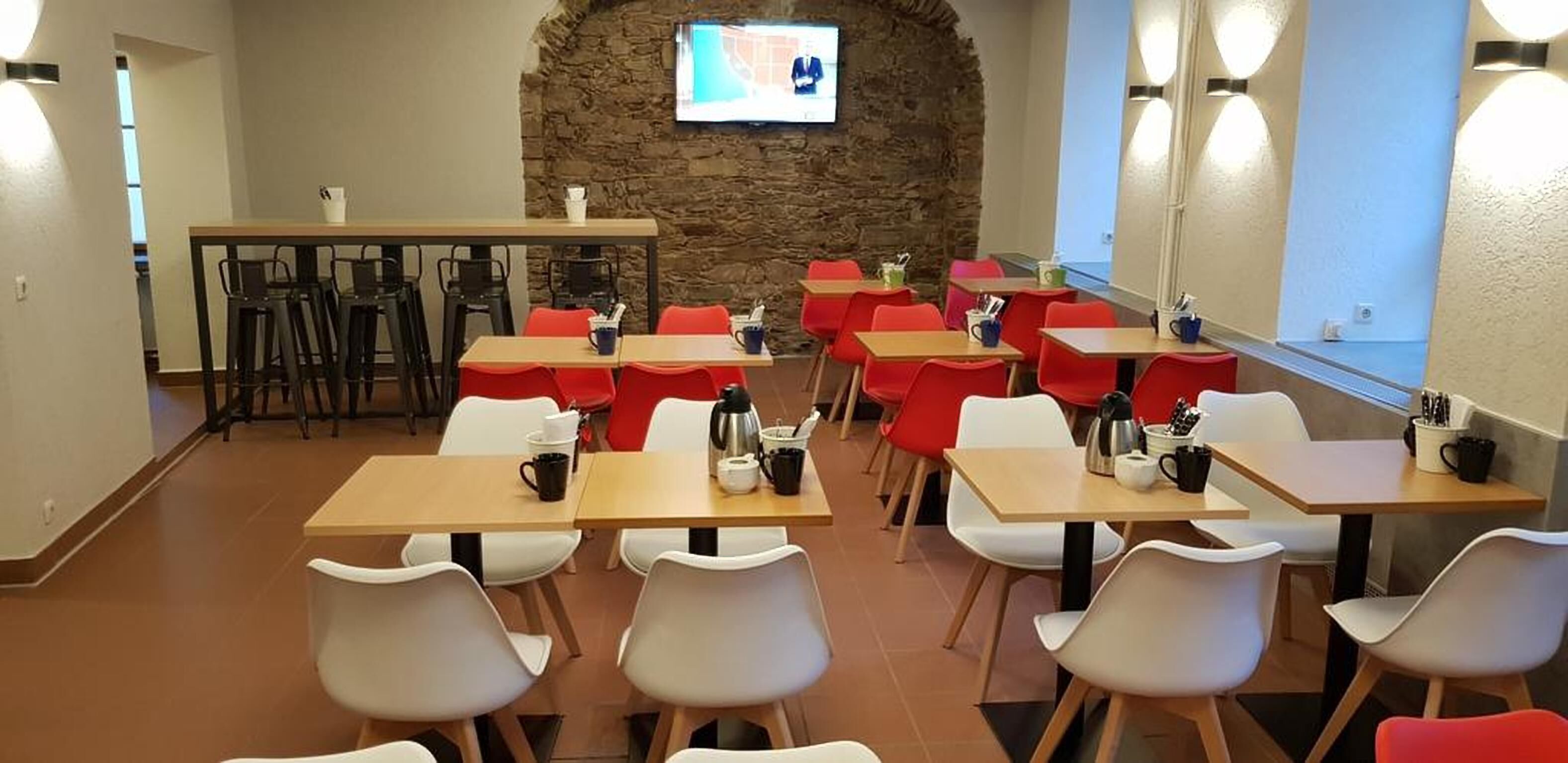 A dining area with tables and chairs, a stone wall, and a television screen.