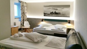 A hotel room with two beds, a view of a forest through a window, a lamp, and a painting on the wall. - Hotel Miriquidi (Oberwiesenthal)
