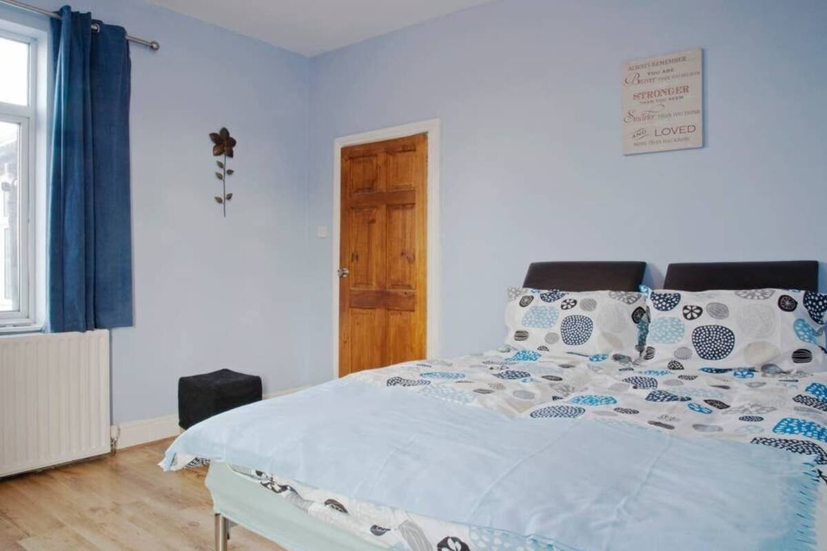 A bedroom with a bed, a window with curtains, a wooden door, and a motivational quote on the wall.