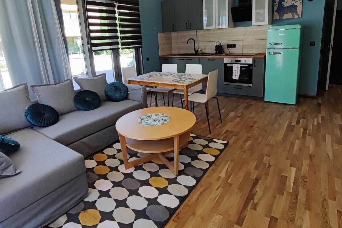 Ein modernes Wohnzimmer mit einer Couch, einem runden Holztisch und einer Küchenzeile mit Schränken und einem Kühlschrank.