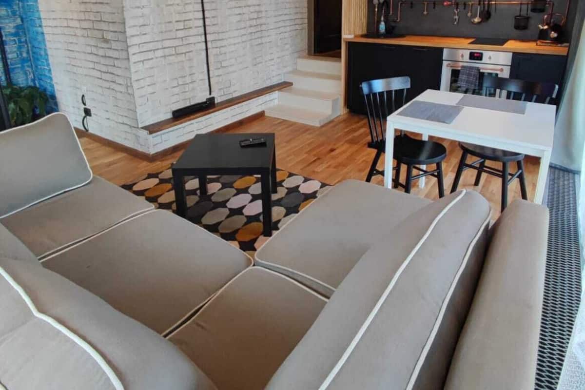 Ein modernes Wohnzimmer mit einem Flachbildfernseher, einem Essbereich mit Tisch und Stühlen sowie einer Küche mit dunklen Schränken und Kupferrohren.