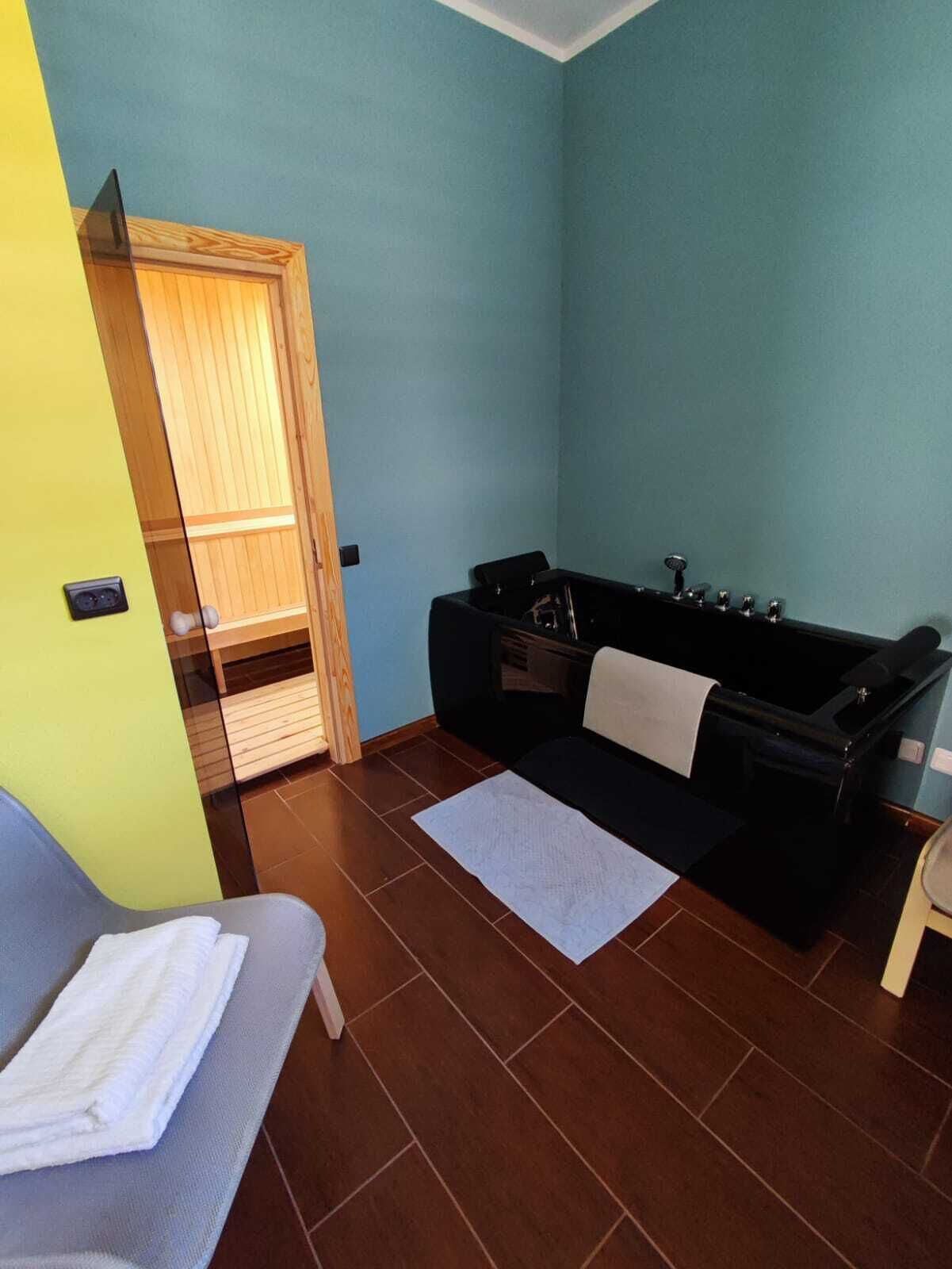 A small room with a wooden door, a black bathtub, a gray sofa, and a white towel on the sofa.