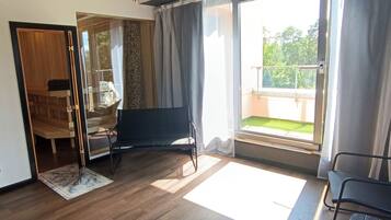 Ein geräumiges Zimmer mit Holzboden, Deckenventilator, großem Fenster mit Vorhängen und Blick ins Freie.