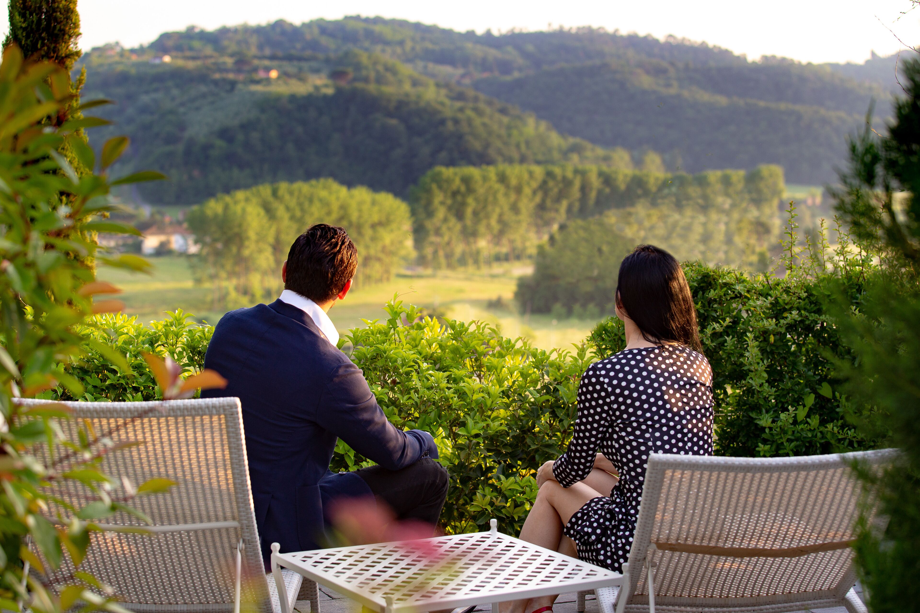 Una pareja sentada en una mesa con vistas a un paisaje verde y exuberante y colinas al fondo.
