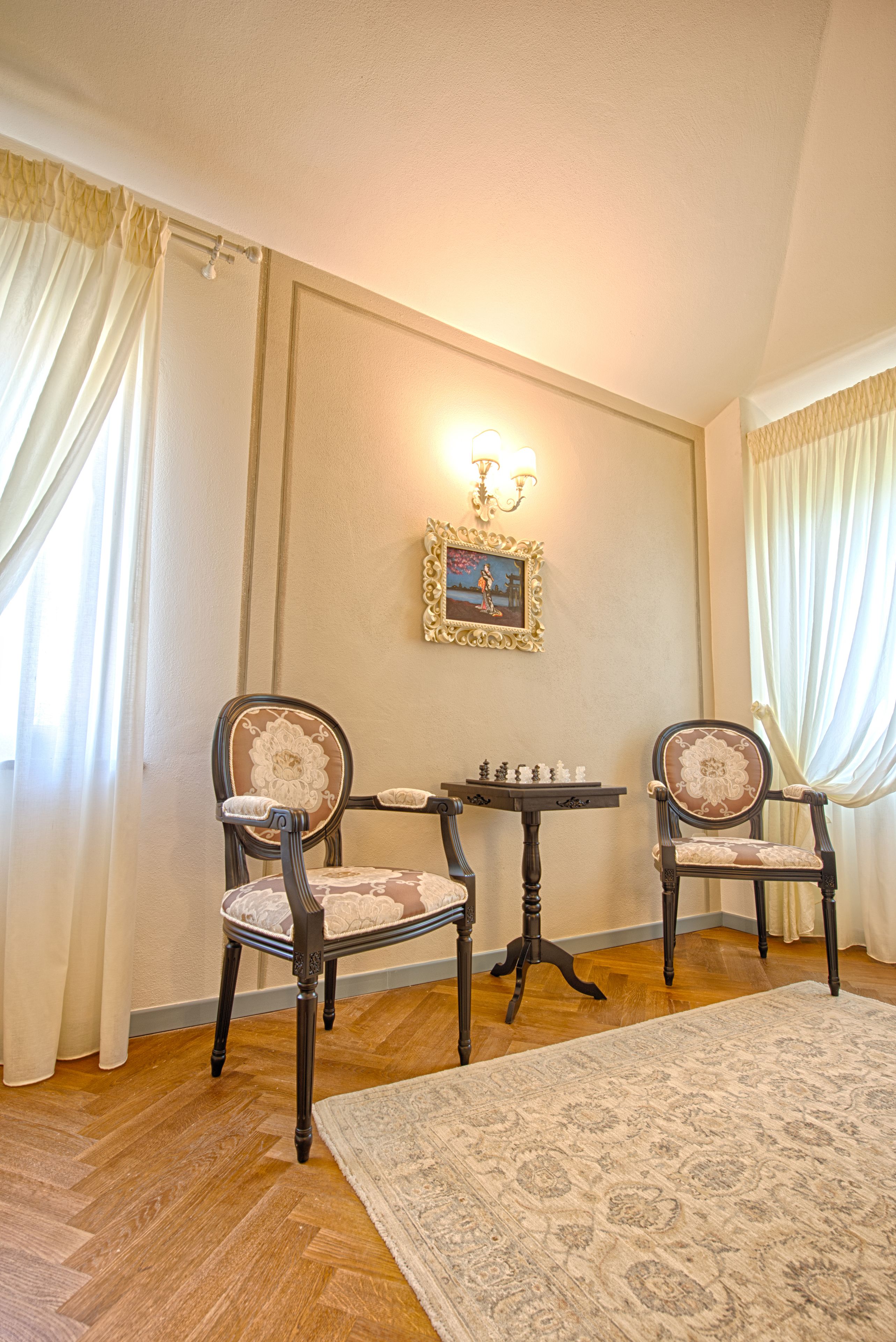 A room with two wooden chairs, a small table, and a framed picture on the wall.
