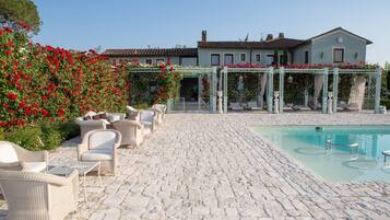 A courtyard with a pool, wicker furniture, and a building with a garden.