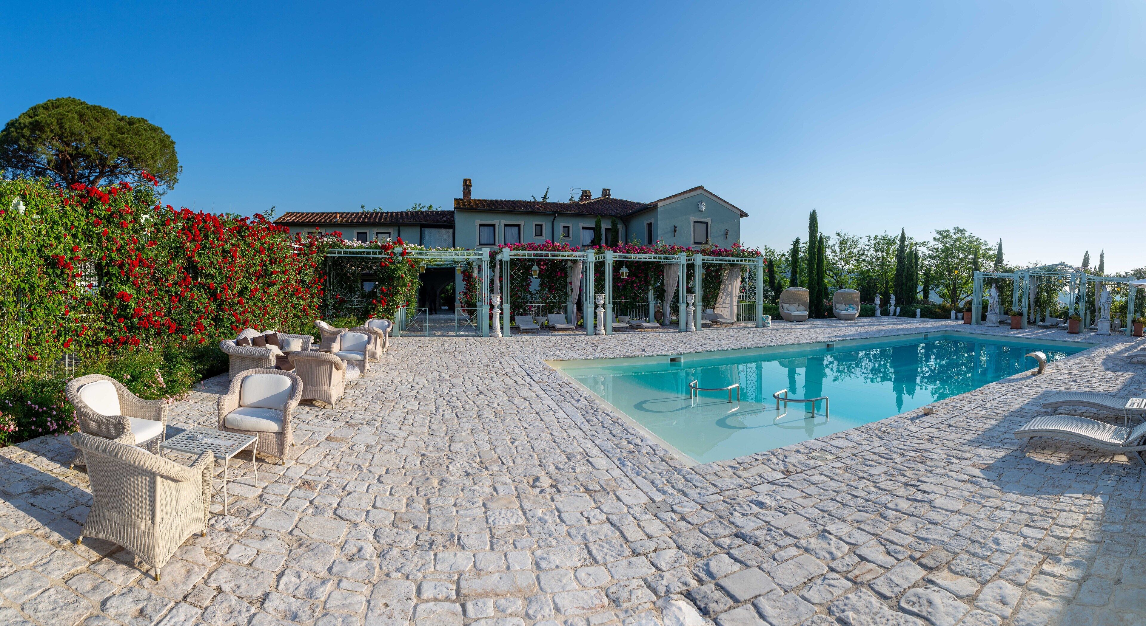 A poolside area with stone flooring, lounge chairs, and a building in the background.