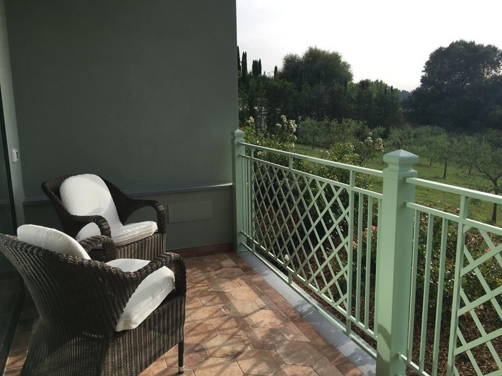 A balcony with wicker chairs and a green railing overlooking a garden.