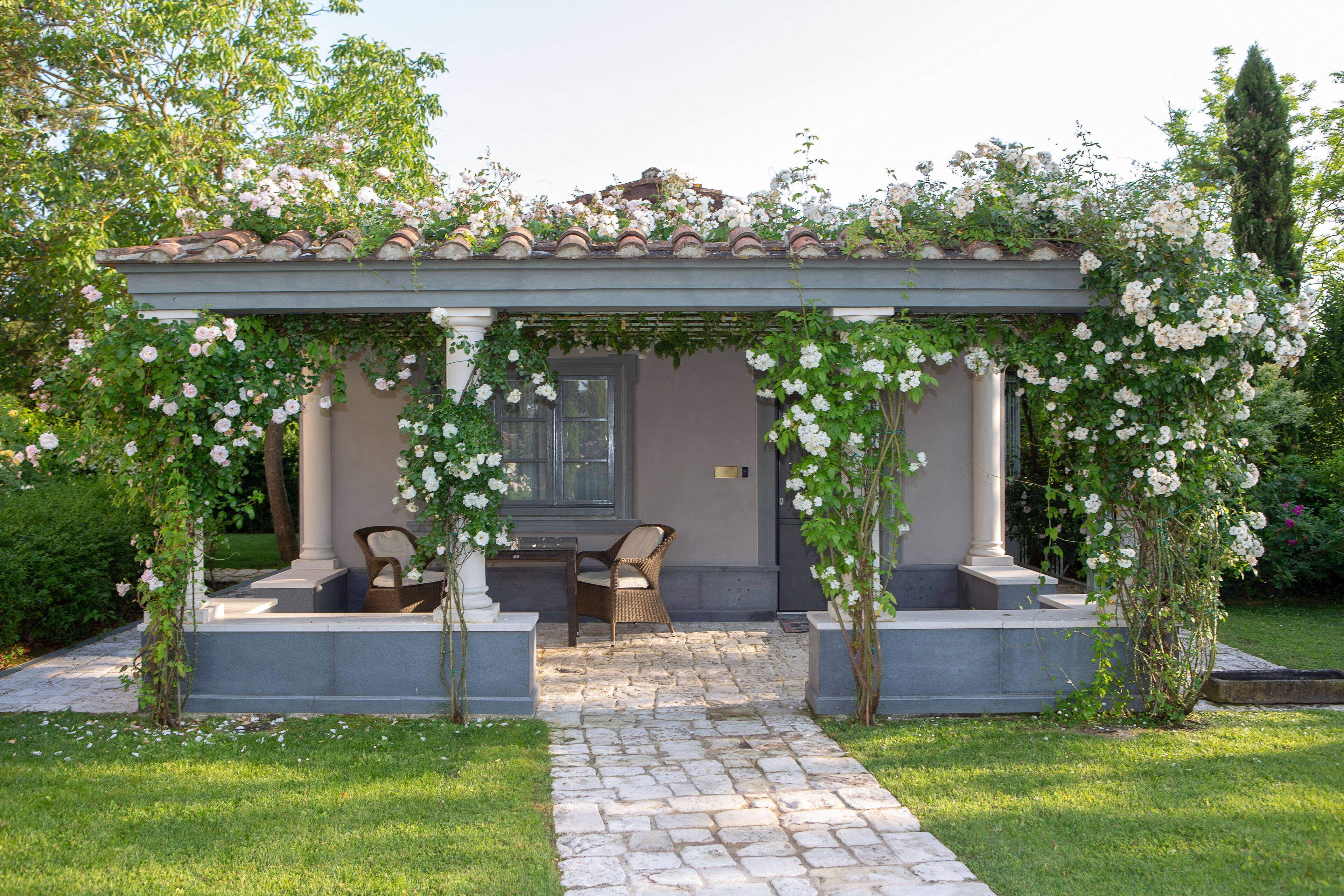 Ein überdachter Außenbereich mit Pergola, Steinweg und zwei Stühlen.