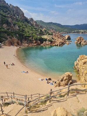 A beach with clear turquoise water, rocky cliffs, and a wooden staircase leading down to the shore. - Hotel Costa Paradiso (Trinità d'Agultu e Vignola)