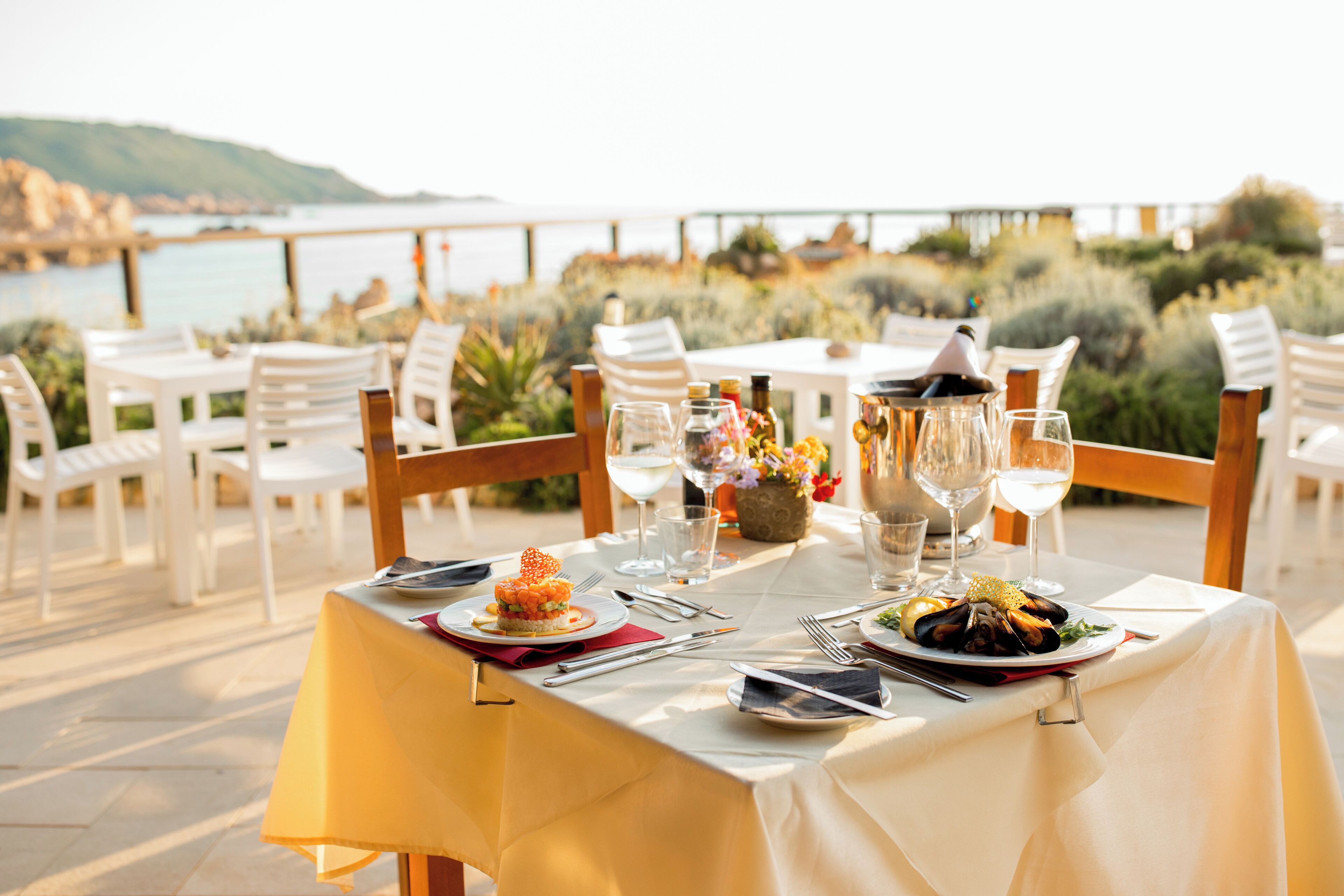 A dining table set outdoors with white chairs, a tablecloth, and dishes.