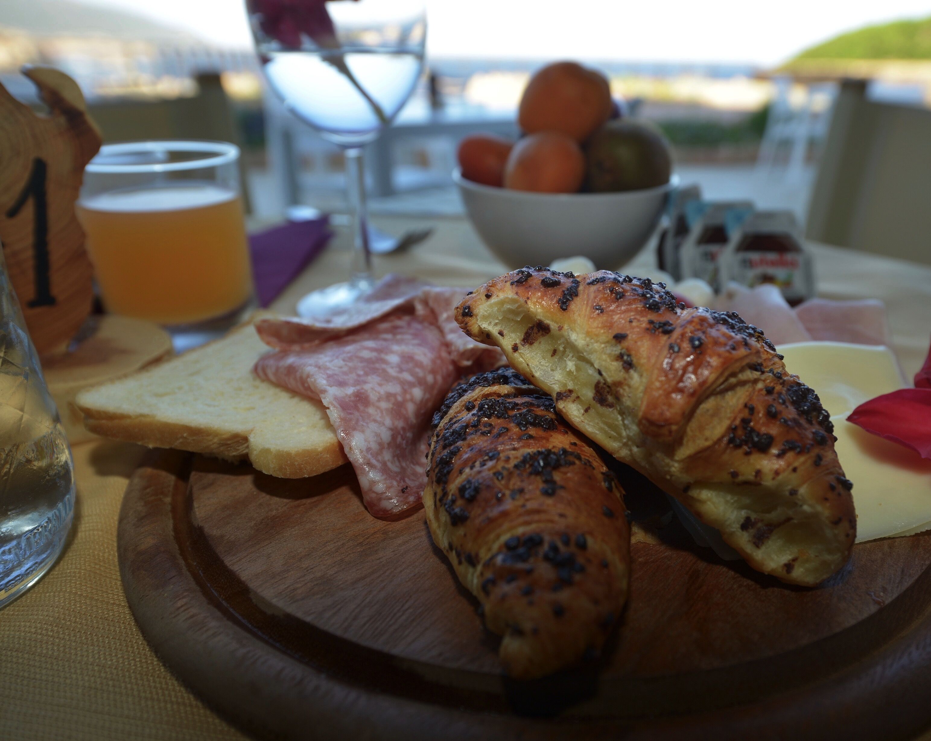 Ein Holzbrett mit Croissants, Brotscheiben und einem Stück Schinken.