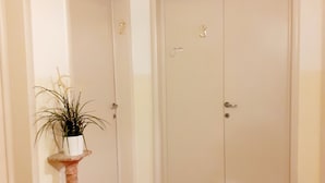A hallway with a clock, two doors, and a potted plant on a pedestal. - Novella Italy (Florence)
