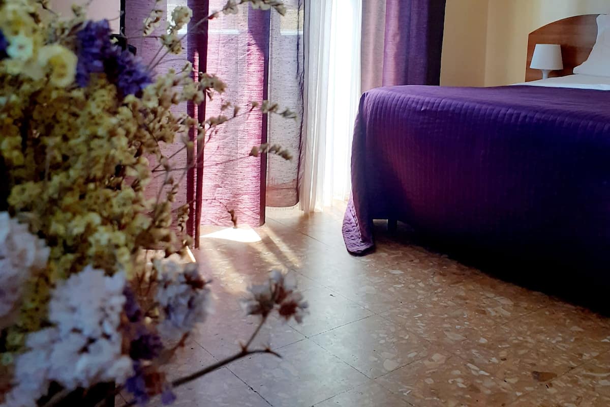 Une pièce avec un lit, une chaise et une fenêtre avec des rideaux.