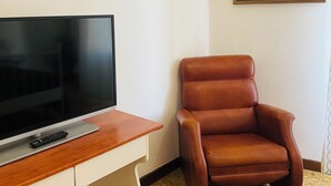 A room with a flat-screen TV on a wooden desk, a brown leather chair, and two framed paintings on the wall. - Novella Italy (Florence)